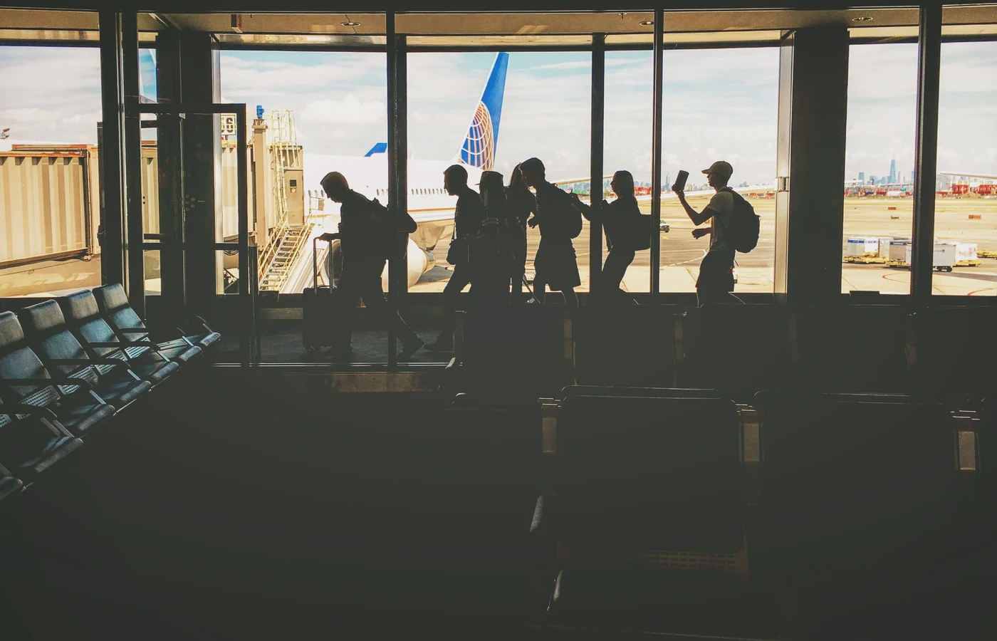Travelers walking through an airport terminal with an airplane visible outside